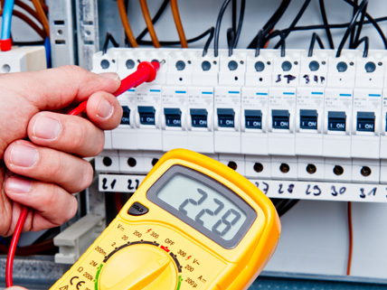 Elektriker prüft mit einem gelben Multimeter die Spannung an einem Sicherungskasten